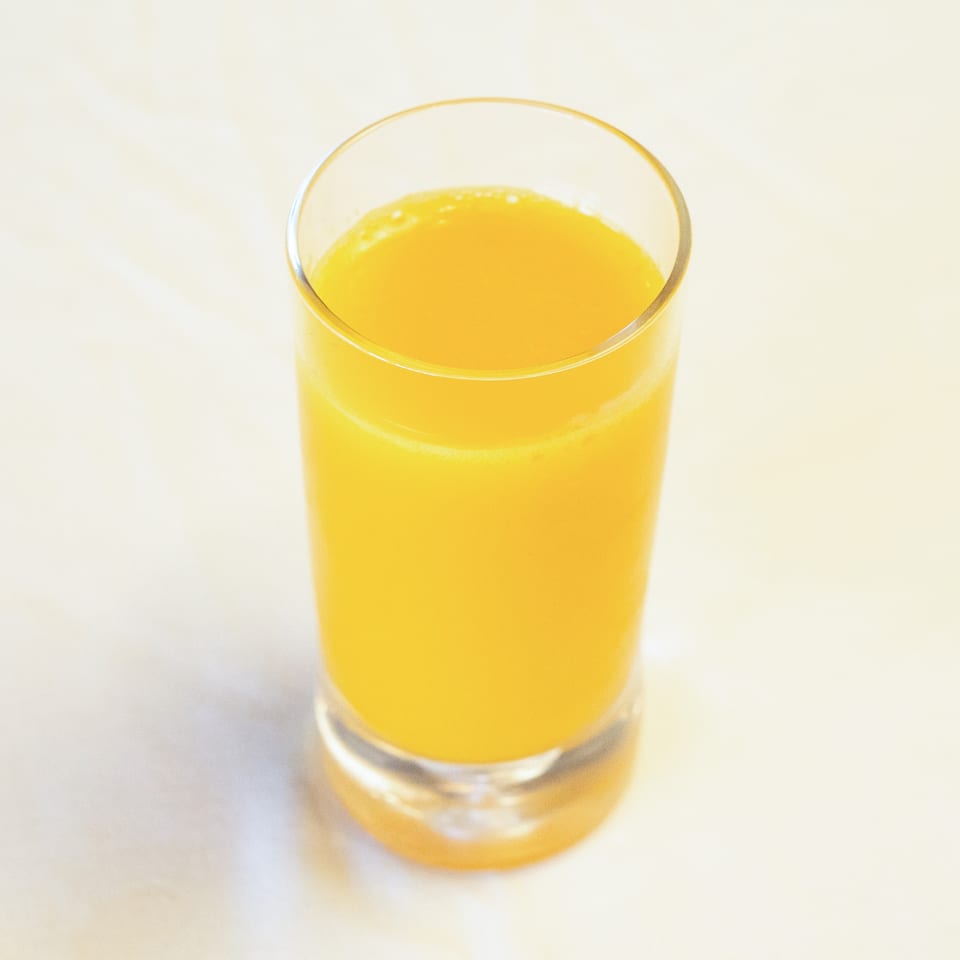 A tall glass filled with bright orange juice on a light background.