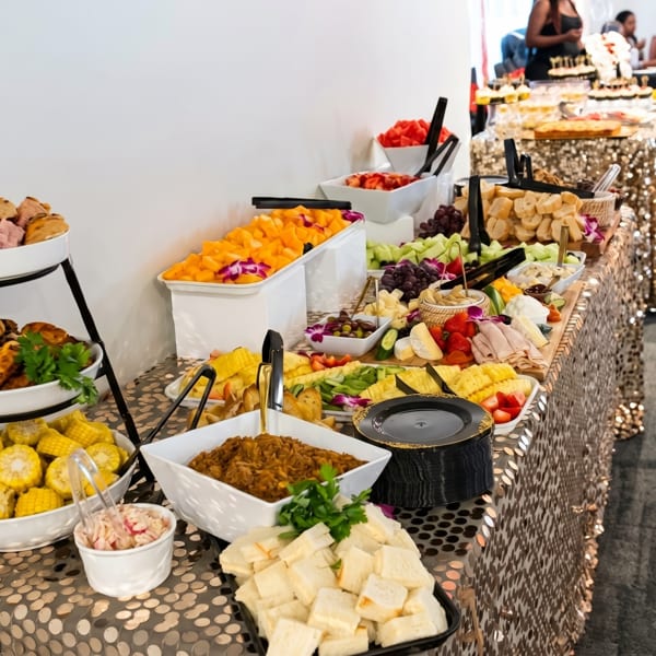 A lavish buffet table covered in gold sequins, laden with fruits, cheeses, meats, and various dishes.