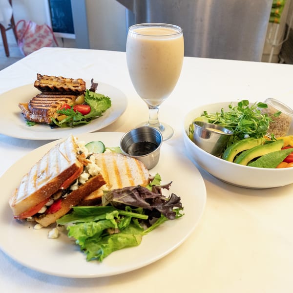 Table set with two grilled sandwiches, a smoothie, and a vibrant salad bowl.